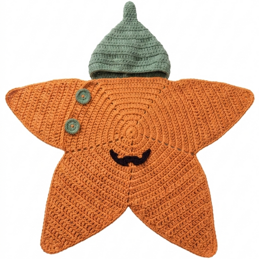 An orange crocheted star-shaped baby pajamas with a green knit hat on top, featuring embroidered facial features and two decorative buttons on the left side, set against a plain white background.